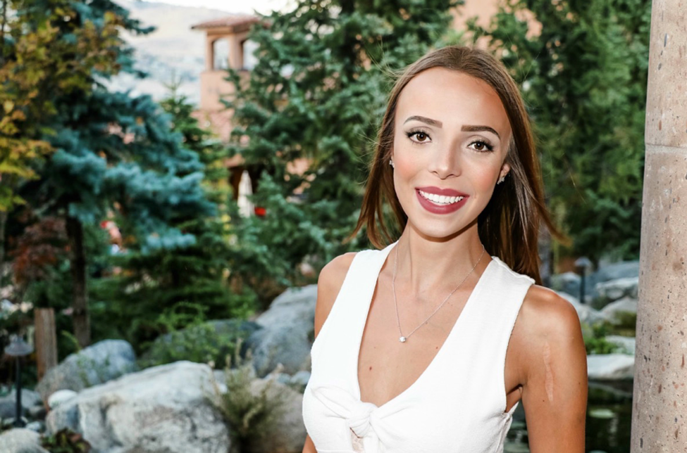 Rachel Meier poses in front of boulders and evergreen trees. She is smiling at the camera.