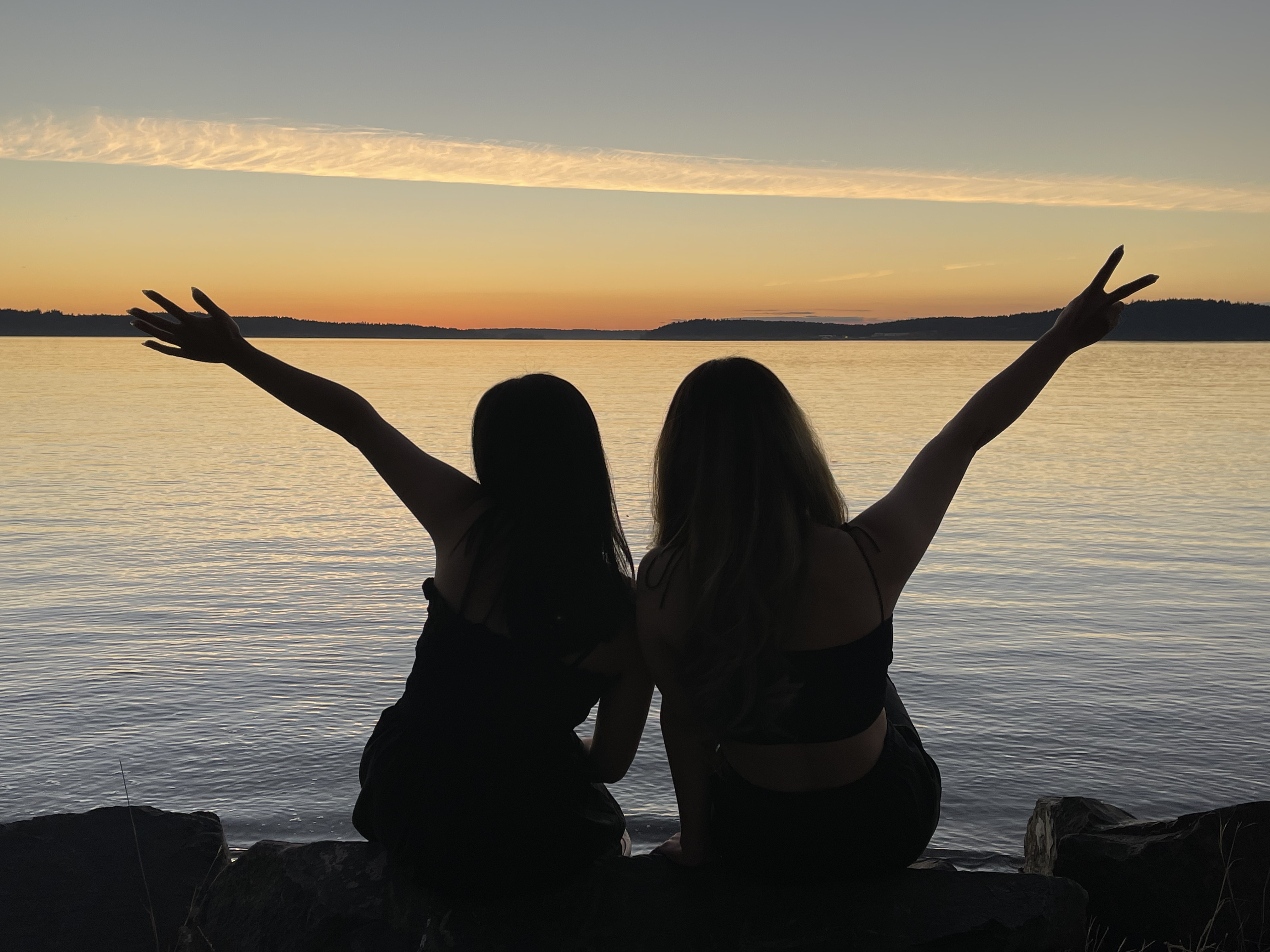 Two girl sitting facing the sunset