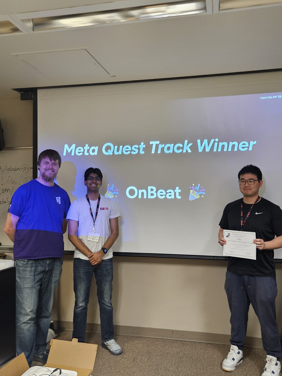 The OnBeat team with their award at the Hack the AM closing ceremony, in front of a screen reading Meta Quest Track Winner